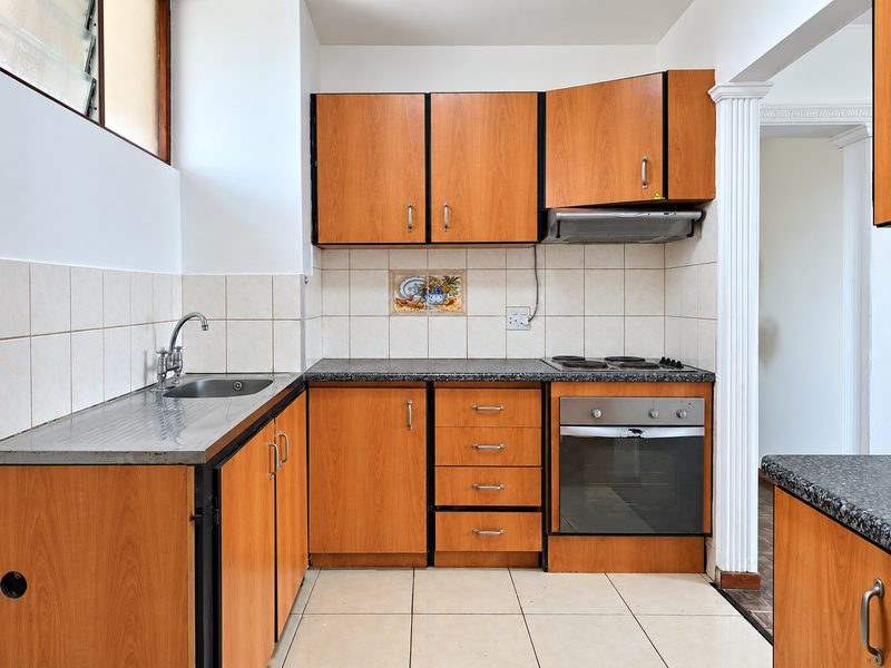 A functional kitchen featuring wood-look cabinetry, built-in oven, electric hob, and tiled finishes, offering a practical layout ready for modern updates.