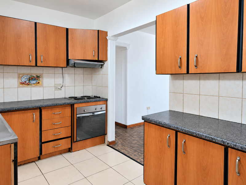 A functional kitchen featuring wood-look laminate cabinetry, dark laminate countertops, built-in oven, electric hob, and neutral ceramic tiling throughout.