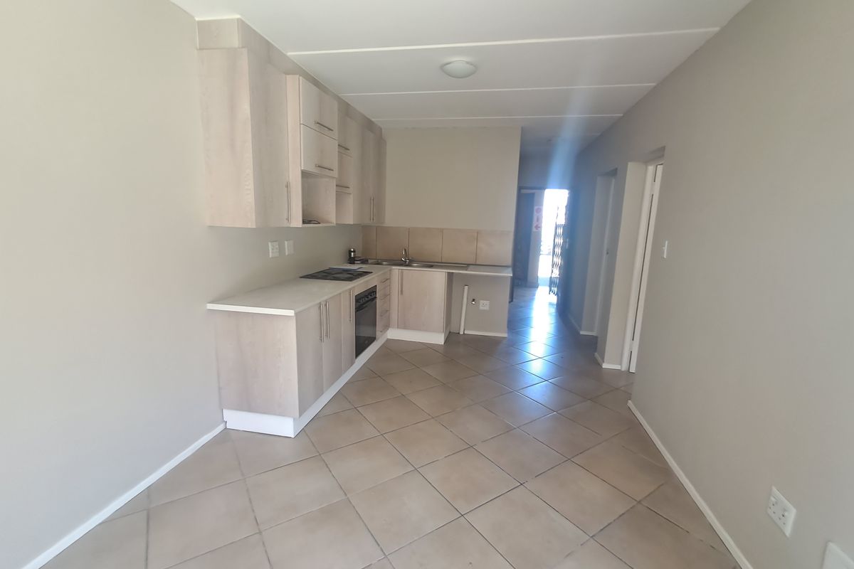 A clean, empty kitchen featuring light wood-look cabinetry, laminate countertops, a built-in oven and hob, and neutral tiled flooring.