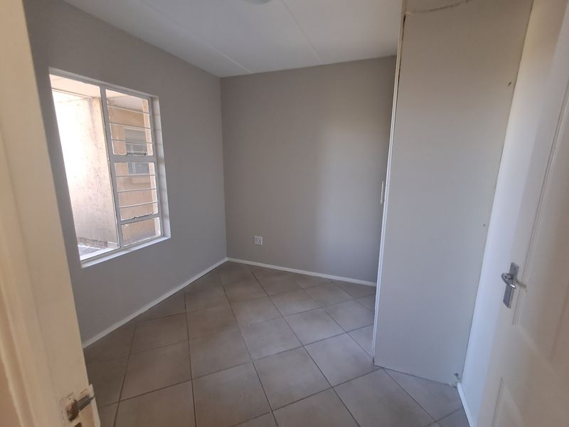 A vacant bedroom featuring neutral wall tones, tiled flooring, and a built-in cupboard, offering a clean canvas for personalization.