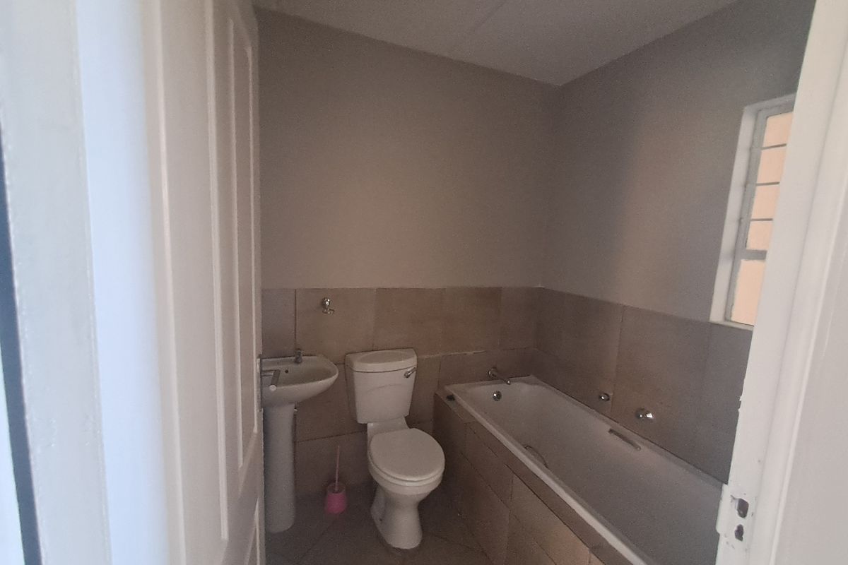 A functional bathroom featuring a pedestal basin, toilet, and a built-in bathtub with tiled surround and splashbacks.