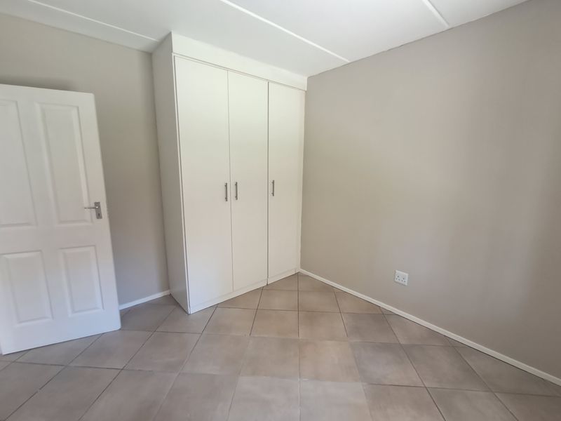 A clean, empty bedroom featuring neutral wall tones, tiled flooring, and built-in white cupboards, offering a versatile space ready for personalization.