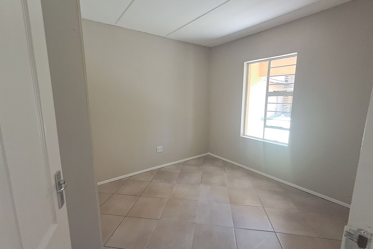 A clean, empty bedroom featuring neutral tiled flooring, a window with security bars, and a simple ceiling light fixture.