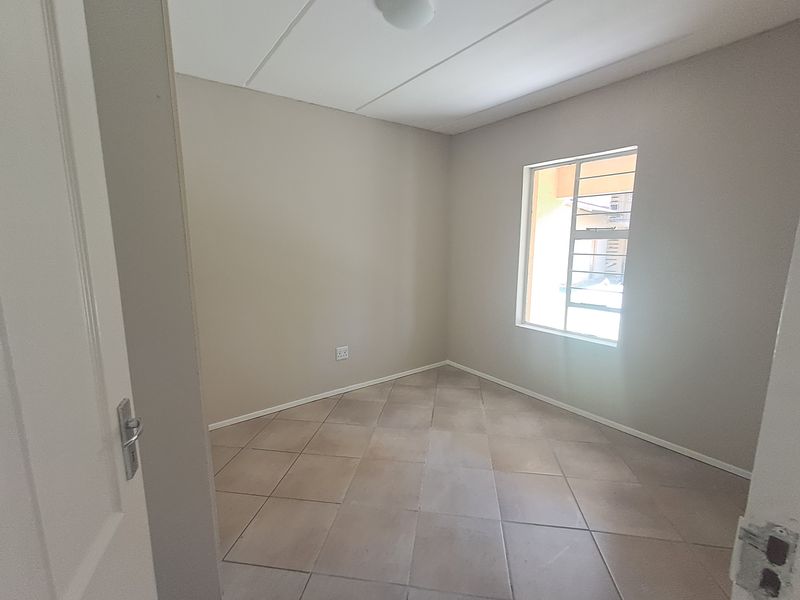 A clean, empty bedroom featuring neutral tiled flooring, a window with security bars, and a simple ceiling light fixture.