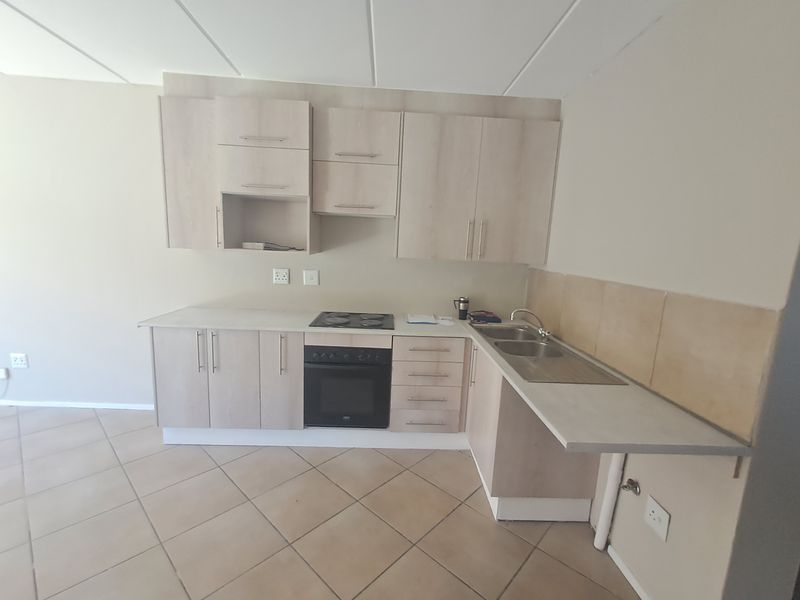 A functional kitchen featuring light wood-finish cabinetry, laminate countertops, a built-in oven and hob, and a double stainless steel sink with tiled splashback.