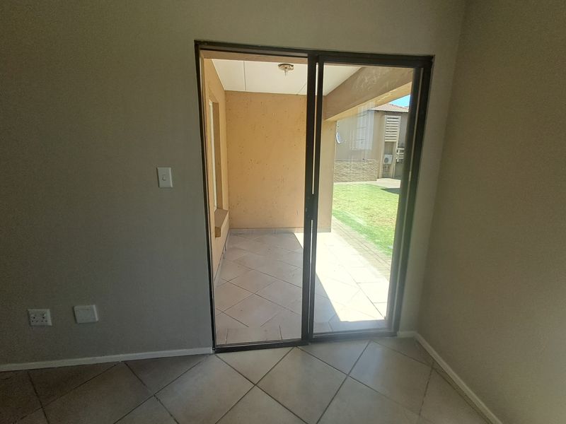 A view from an interior room through a sliding glass door onto a covered patio with tiled flooring and access to a small garden area.
