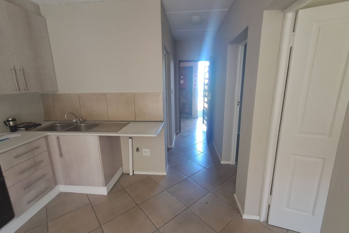 A functional kitchen area featuring built-in cabinetry, a stainless steel sink, and tiled flooring, leading into a hallway with access to other rooms.