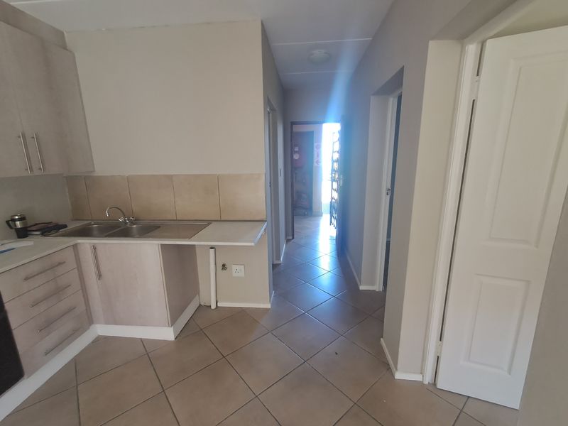 A functional kitchen area featuring built-in cabinetry, a stainless steel sink, and tiled flooring, leading into a hallway with access to other rooms.