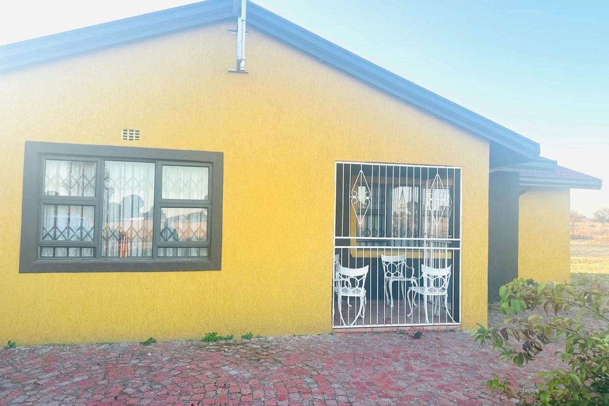 Rear exterior view of a farm property featuring a textured yellow facade, security bars on windows, and a paved outdoor area.