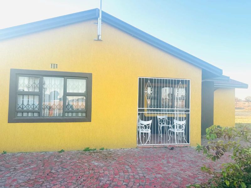 Rear exterior view of a farm property featuring a textured yellow facade, security bars on windows, and a paved outdoor area.