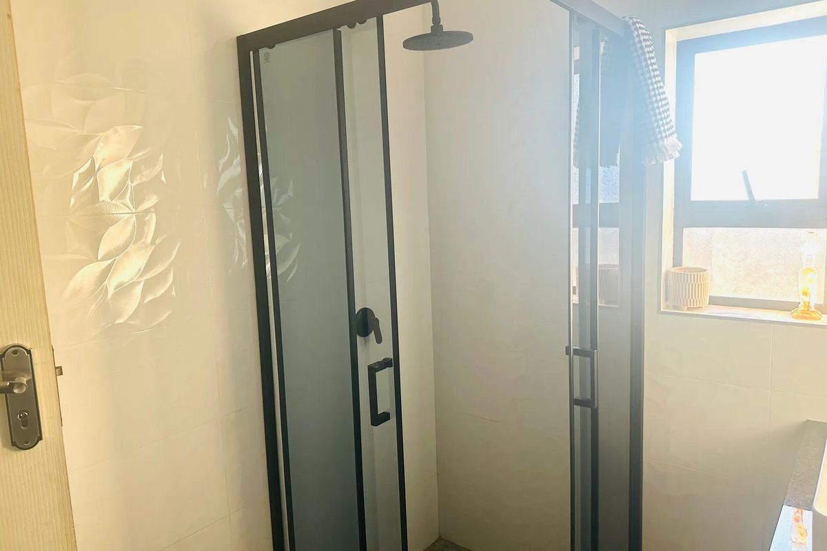 A modern bathroom featuring a sleek black-framed shower enclosure with tiled walls and natural light from a side window.