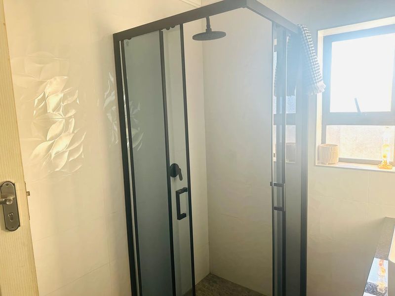 A modern bathroom featuring a sleek black-framed shower enclosure with tiled walls and natural light from a side window.