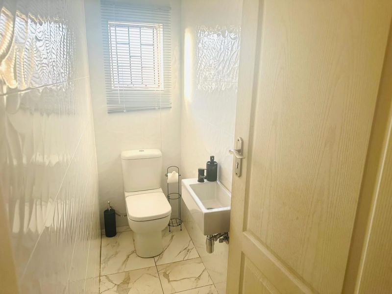 A compact, well-maintained guest bathroom featuring modern tiled walls, marble-look floor tiles, a wall-mounted basin, and a window with fitted blinds.