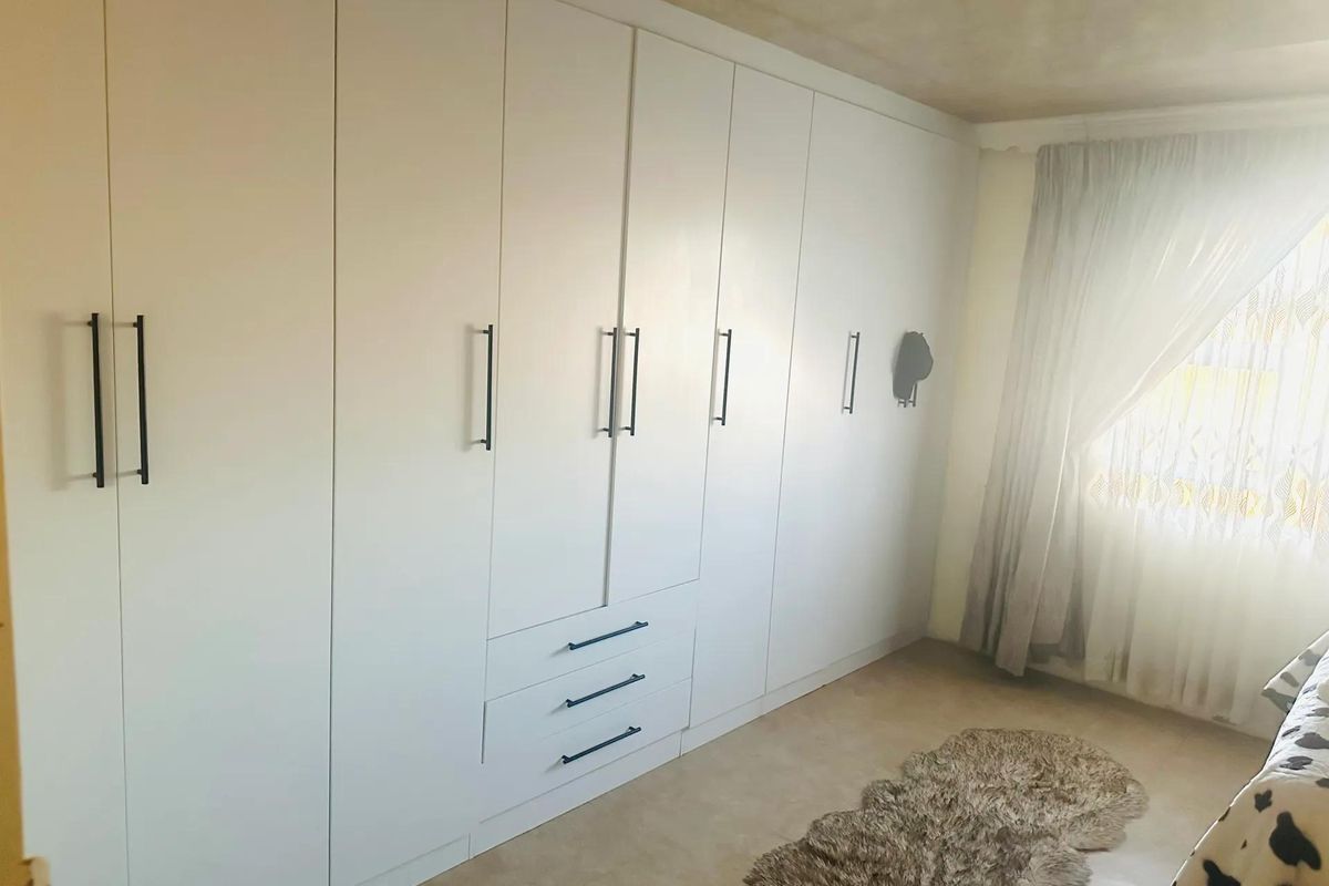 A bedroom featuring extensive white built-in floor-to-ceiling wardrobes with modern dark handles and neutral tiled flooring.