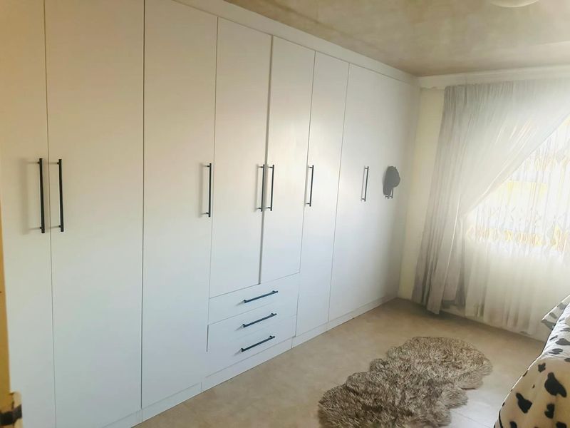 A bedroom featuring extensive white built-in floor-to-ceiling wardrobes with modern dark handles and neutral tiled flooring.