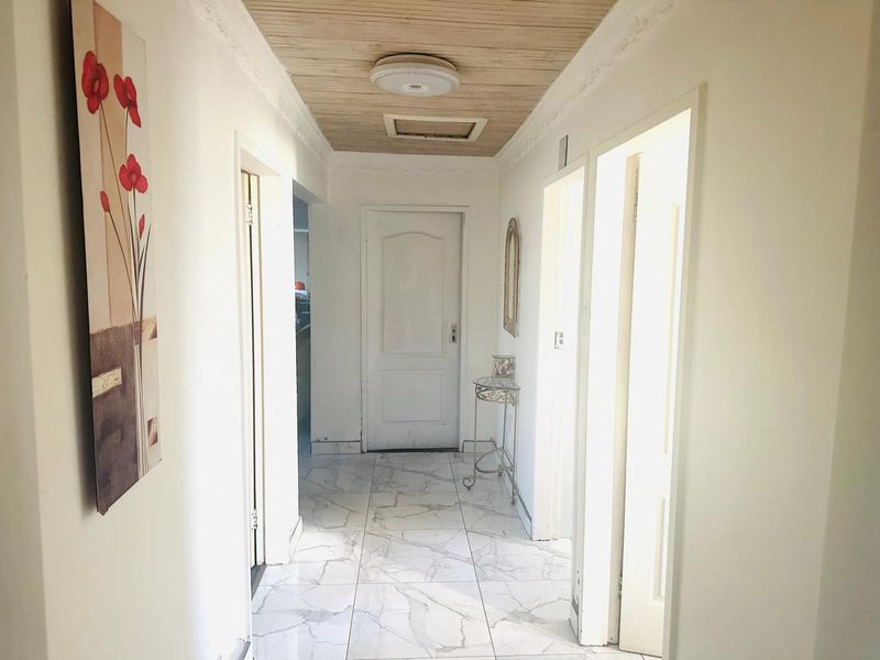 A bright hallway featuring marble-look floor tiles, timber-look ceiling paneling, and multiple doorways leading to adjacent rooms.