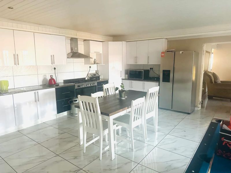 Spacious open-plan kitchen featuring modern white cabinetry, stone countertops, gas hob, and tiled flooring, seamlessly integrated with a dining area.