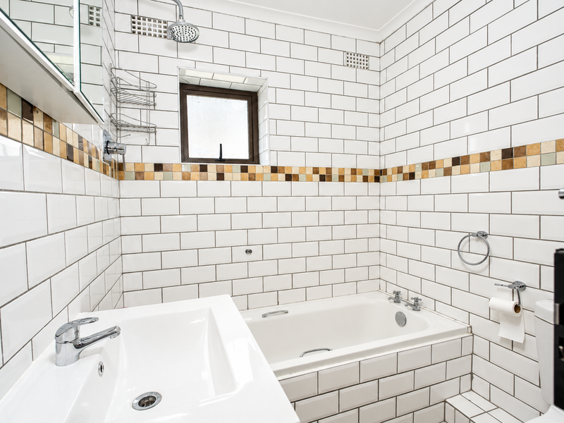 A compact bathroom featuring white subway wall tiles with a decorative mosaic border, a built-in bathtub, and a modern vanity basin.