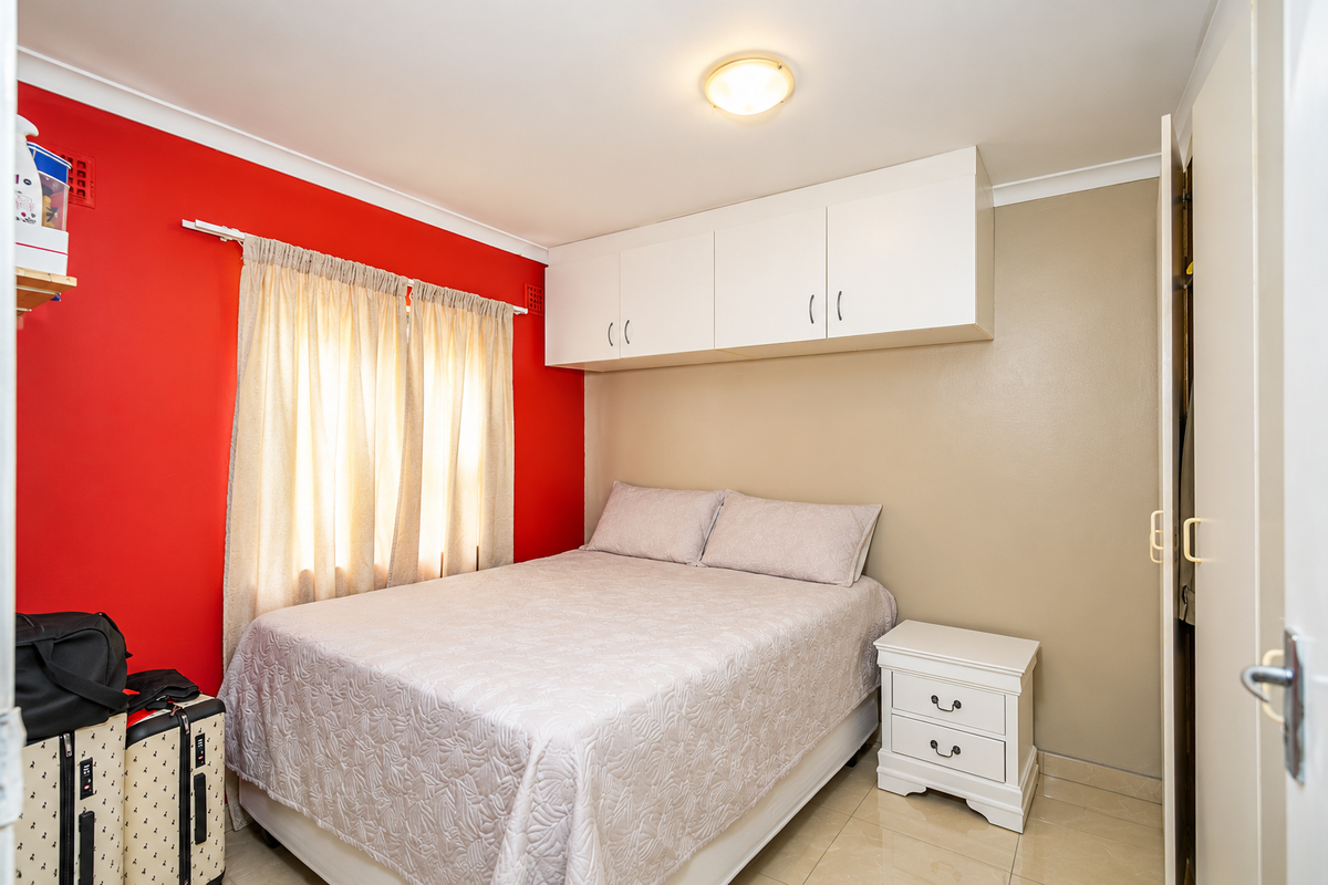 A bedroom featuring tiled flooring, built-in overhead storage cabinetry, and a window with curtain rod, finished with a bold accent wall.