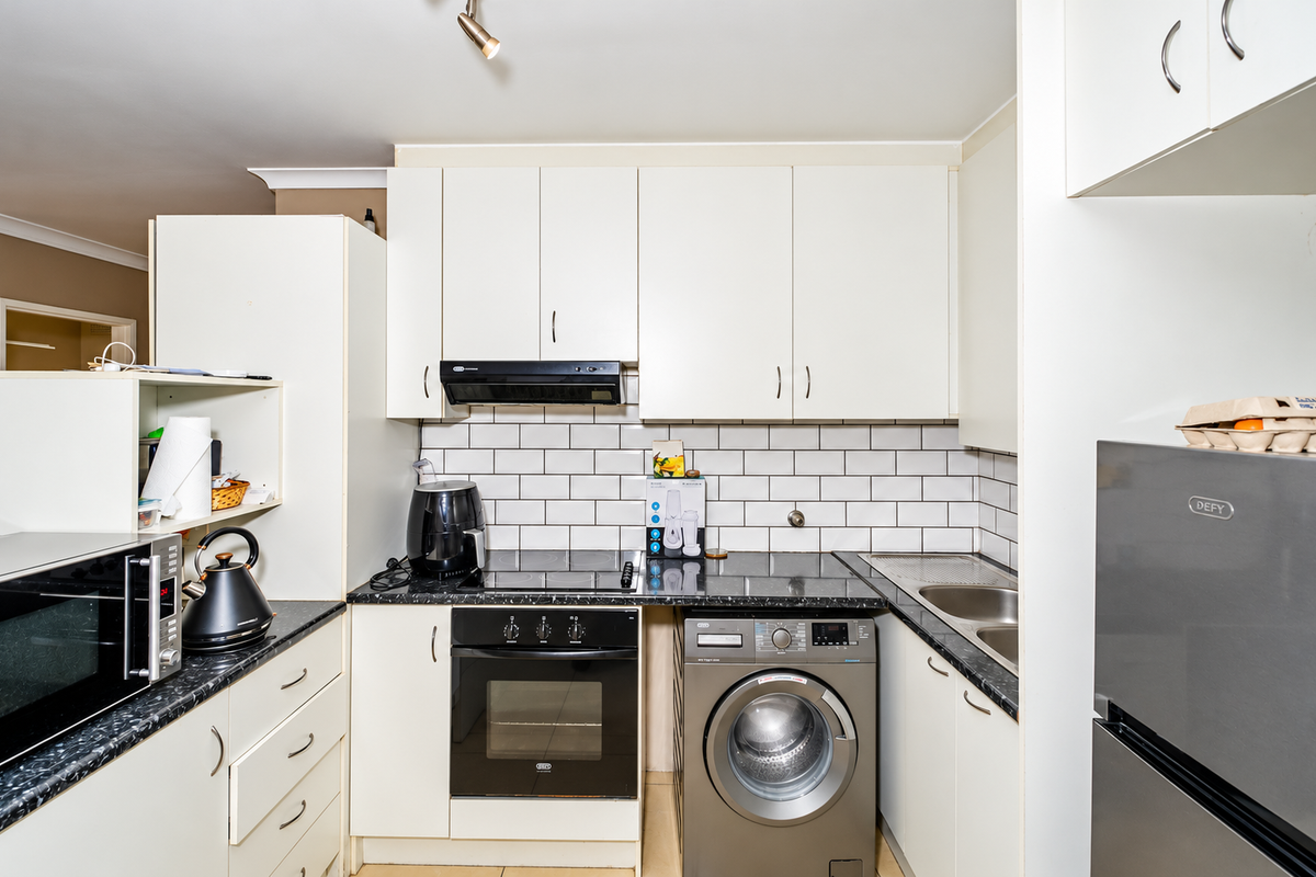 A functional kitchen featuring white cabinetry, subway tile backsplash, dark laminate countertops, integrated oven, hob, extractor fan, and a built-in washing machine.