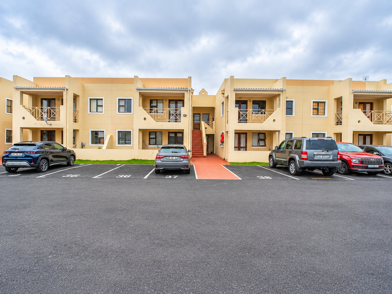 Front elevation of a multi-story apartment complex featuring designated parking bays, private balconies, and external stair access.