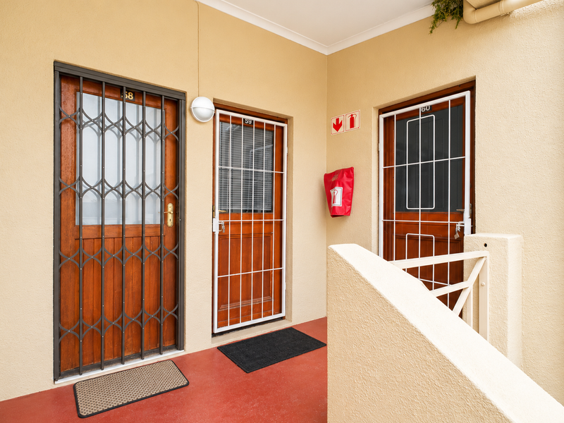 Entrance area featuring three timber doors with security gates, a fire extinguisher, and a balustrade on a communal walkway.