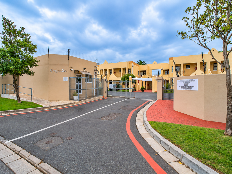 The entrance to Greyville apartment complex featuring secure gated access, electric fencing, and well-maintained paved driveways and landscaped grounds.