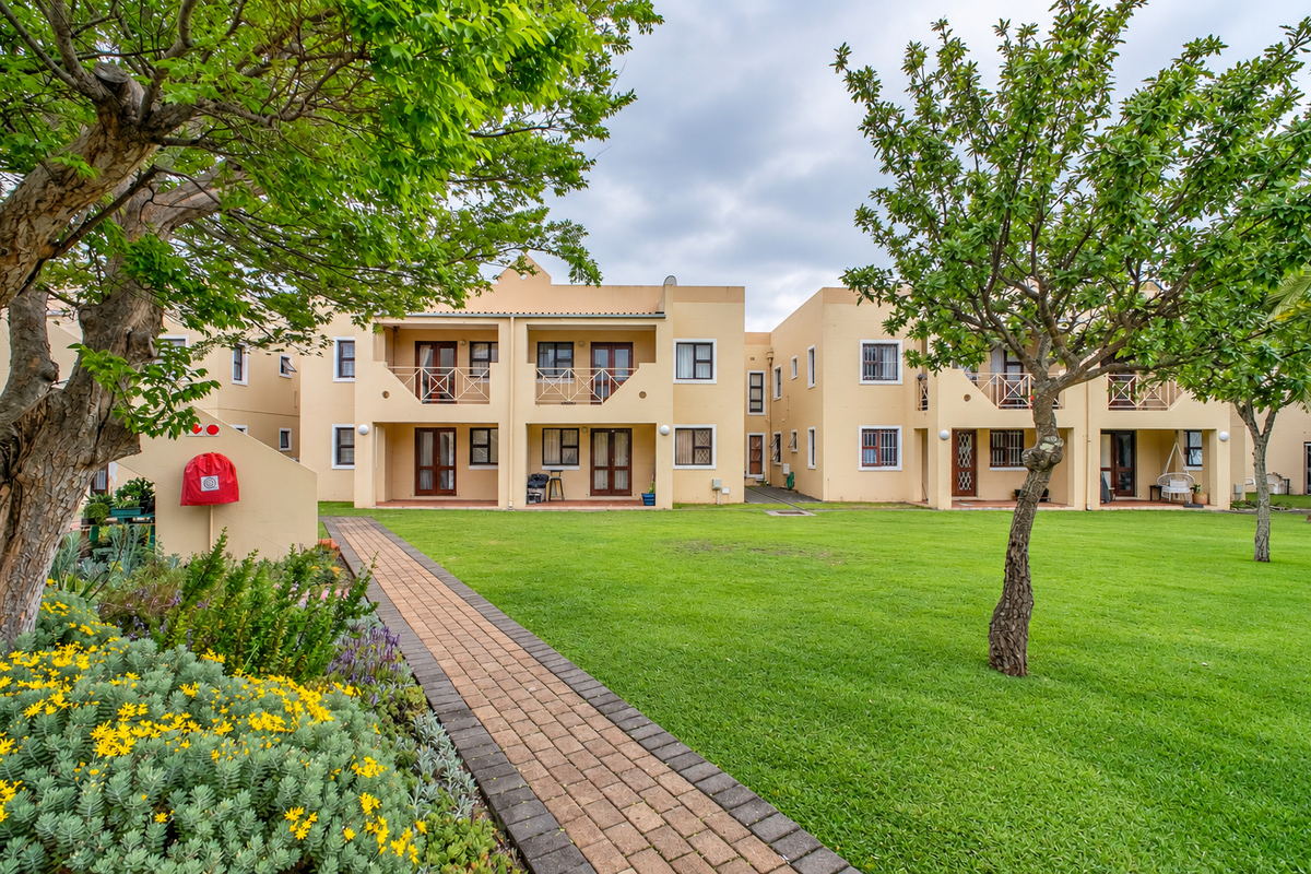 A well-maintained apartment complex exterior featuring a lush green lawn, paved walkway, and private balconies with sliding door access.