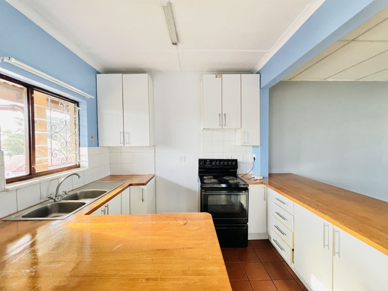 A functional kitchen featuring white cabinetry, wooden countertops, a double basin sink, and a freestanding stove with tiled backsplash and flooring.