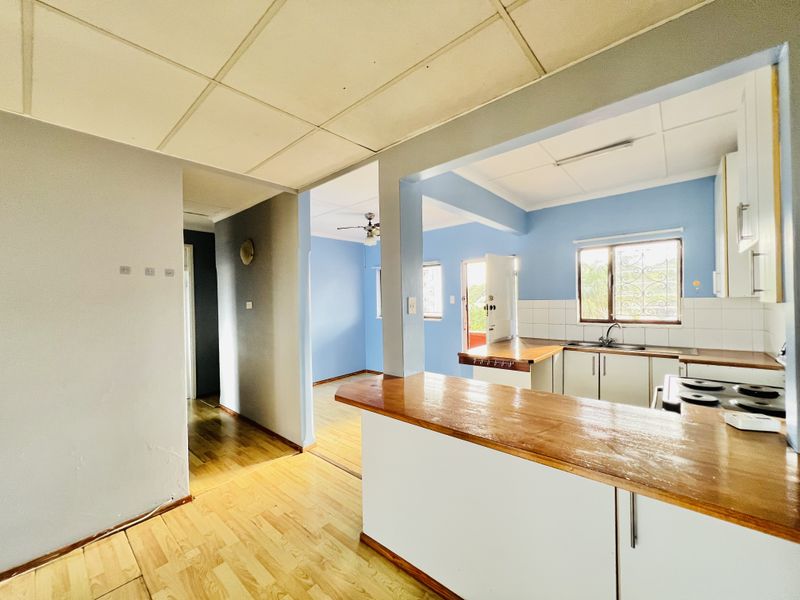 Open plan kitchen and living area featuring laminate flooring, a wooden breakfast bar, and functional built-in cabinetry with a tiled backsplash.