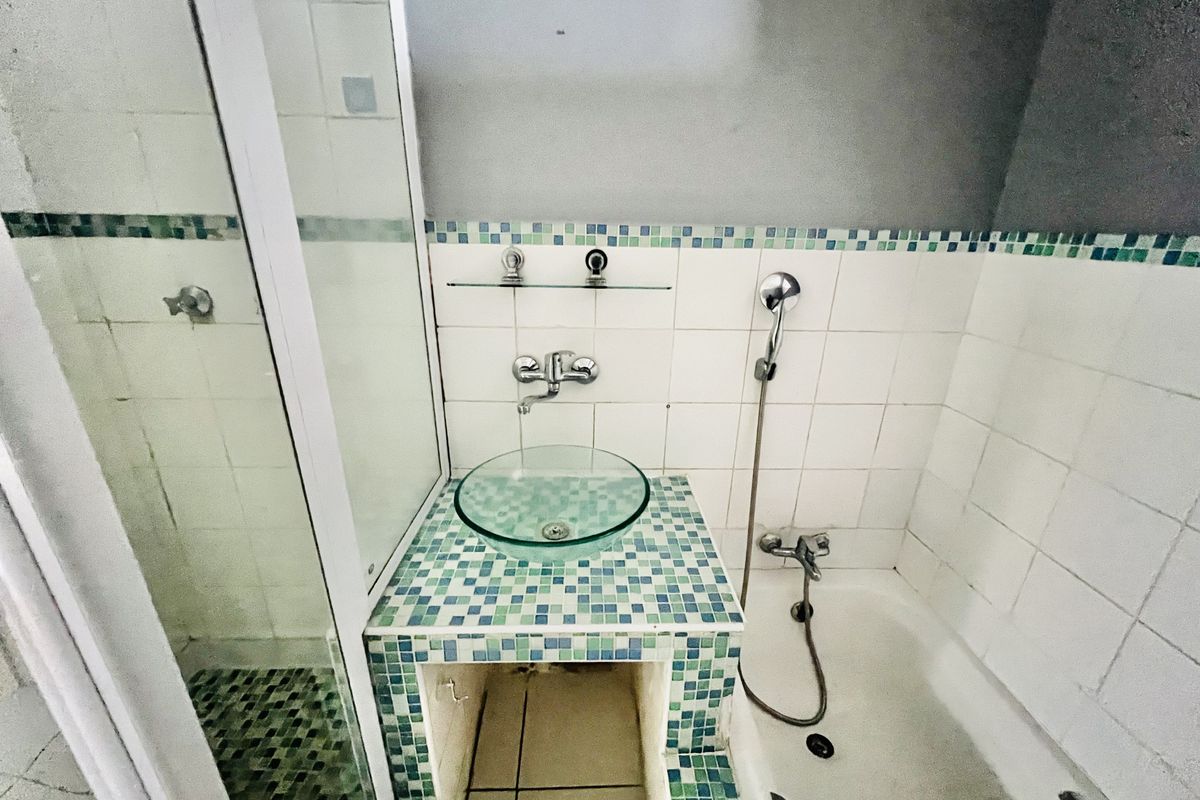 A dated bathroom featuring a glass vessel sink on a mosaic tiled vanity, a shower enclosure, and a bathtub with wall-mounted fixtures.