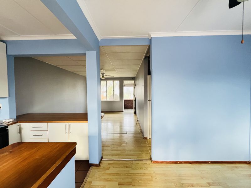 Open plan living area featuring a kitchen with wooden countertops, laminate flooring, and a neutral blue color scheme, leading to a bright adjacent space.