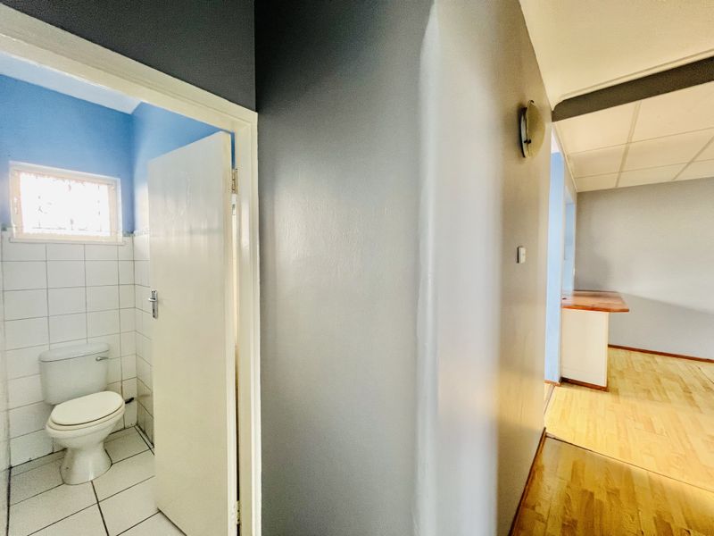 A view from the hallway looking into a tiled bathroom and an adjacent open-plan living area with laminate flooring and a built-in counter.