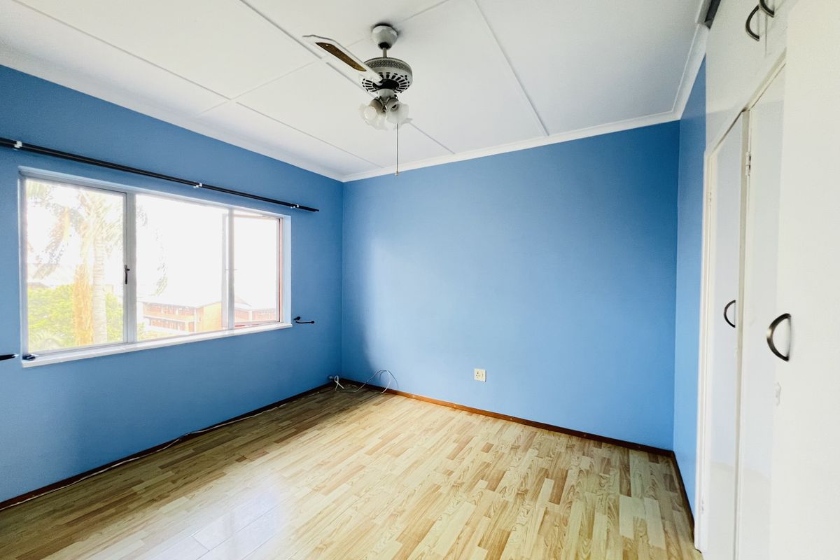 An empty bedroom featuring laminate flooring, built-in cupboards, and a ceiling fan, offering a blank canvas for personalization.
