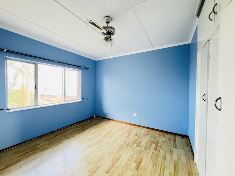 An empty bedroom featuring laminate flooring, built-in cupboards, and a ceiling fan, offering a blank canvas for personalization.