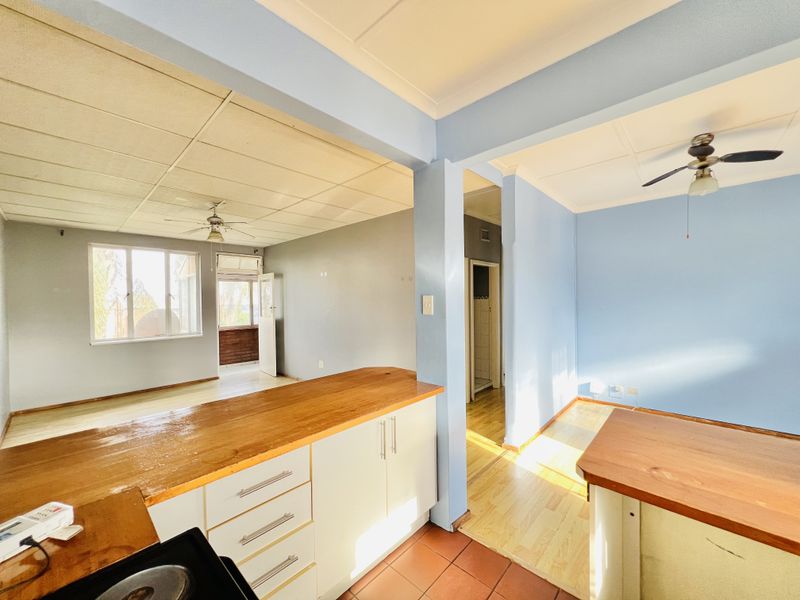 Open plan living and kitchen area featuring wooden countertops, ceiling fans, and a mix of tiled and laminate flooring in a bright, vacant space.