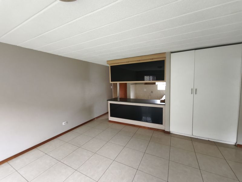 An open-plan living area featuring tiled flooring, a built-in breakfast bar with a pass-through window, and integrated white storage cupboards.