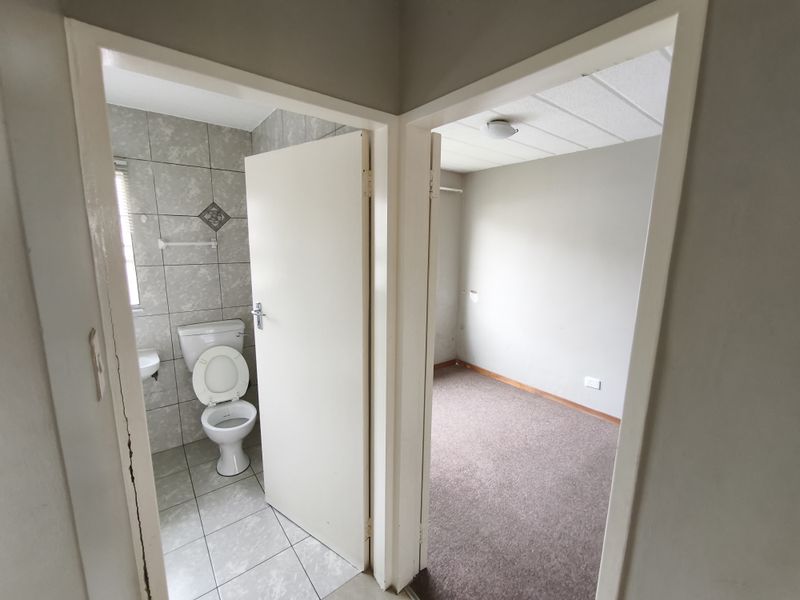 A view from a hallway looking into a tiled bathroom and an empty carpeted bedroom with neutral wall finishes.