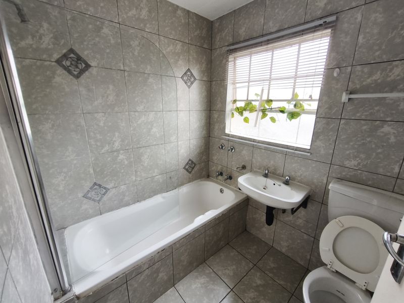 A functional bathroom featuring a built-in bathtub, wall-mounted basin, and toilet, finished with neutral wall and floor tiling.