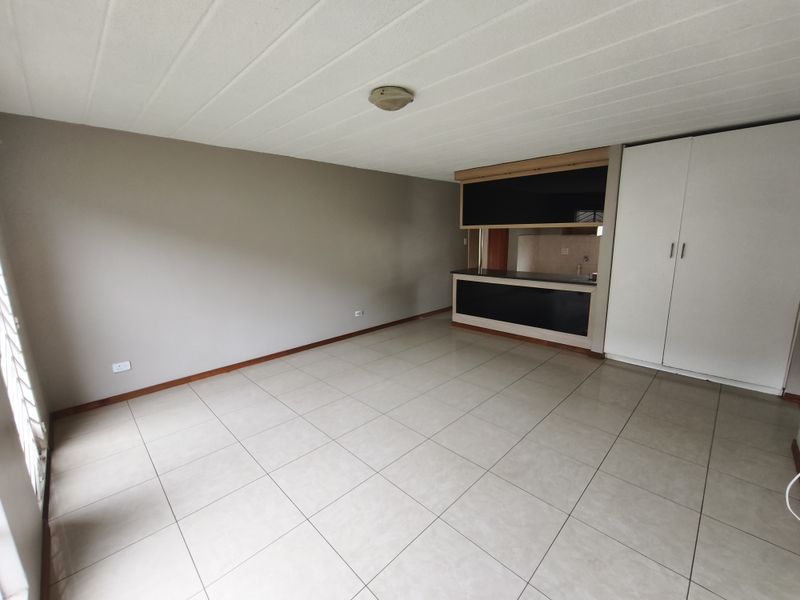 An open-plan living area featuring neutral tiled flooring, a built-in kitchen breakfast bar, and integrated storage cupboards.