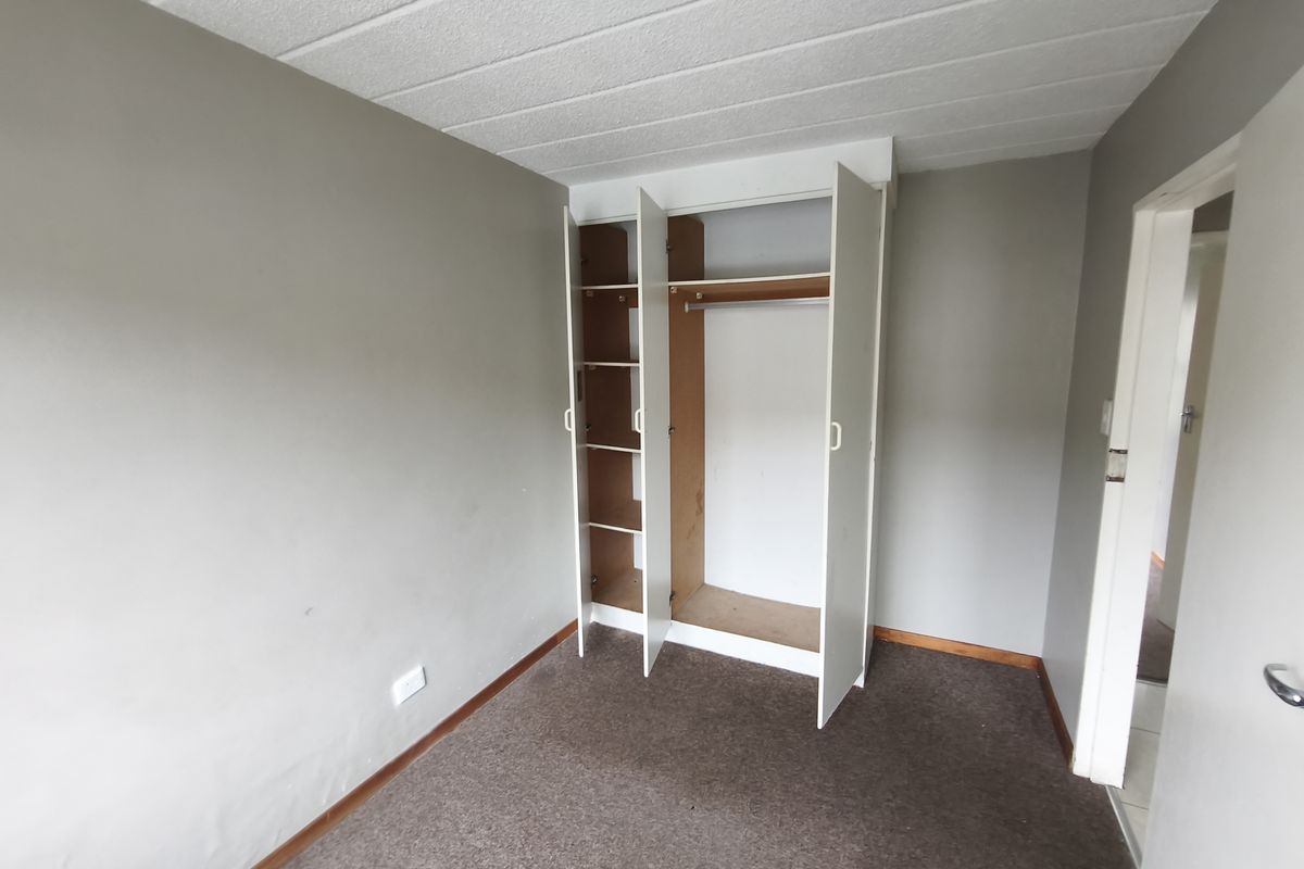An empty bedroom featuring a built-in wardrobe, carpeted flooring, and neutral wall finishes, offering a blank canvas for personalization.