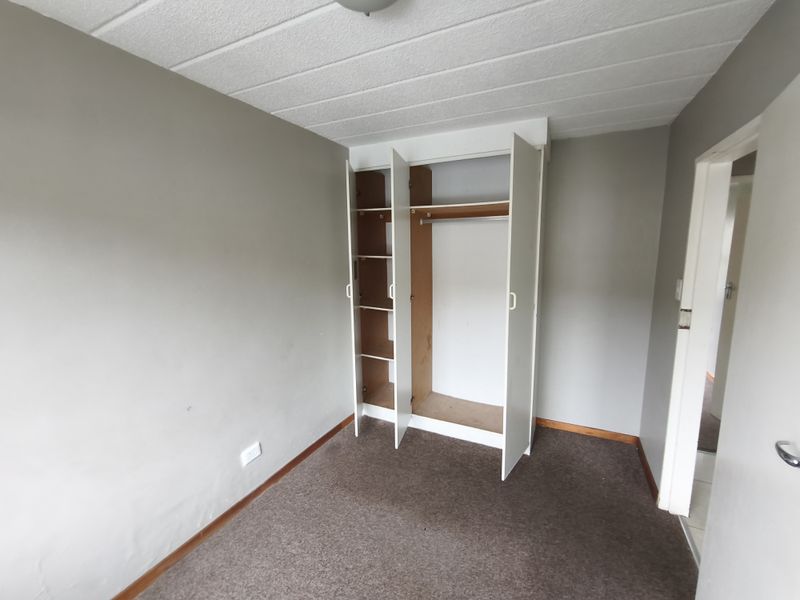 An empty bedroom featuring a built-in wardrobe, carpeted flooring, and neutral wall finishes, offering a blank canvas for personalization.