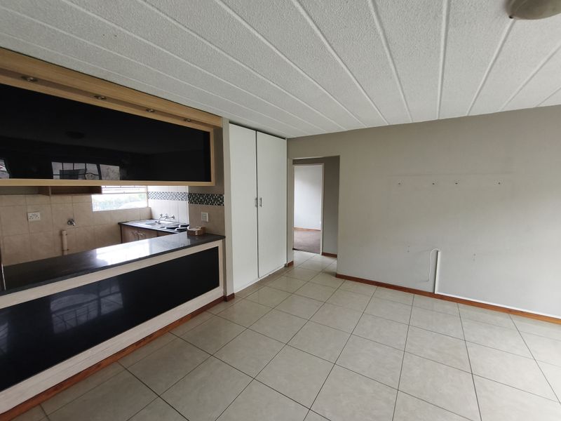 An open-plan living and kitchen area featuring tiled flooring, built-in cabinetry, and a breakfast counter, presenting a functional space ready for personalization.