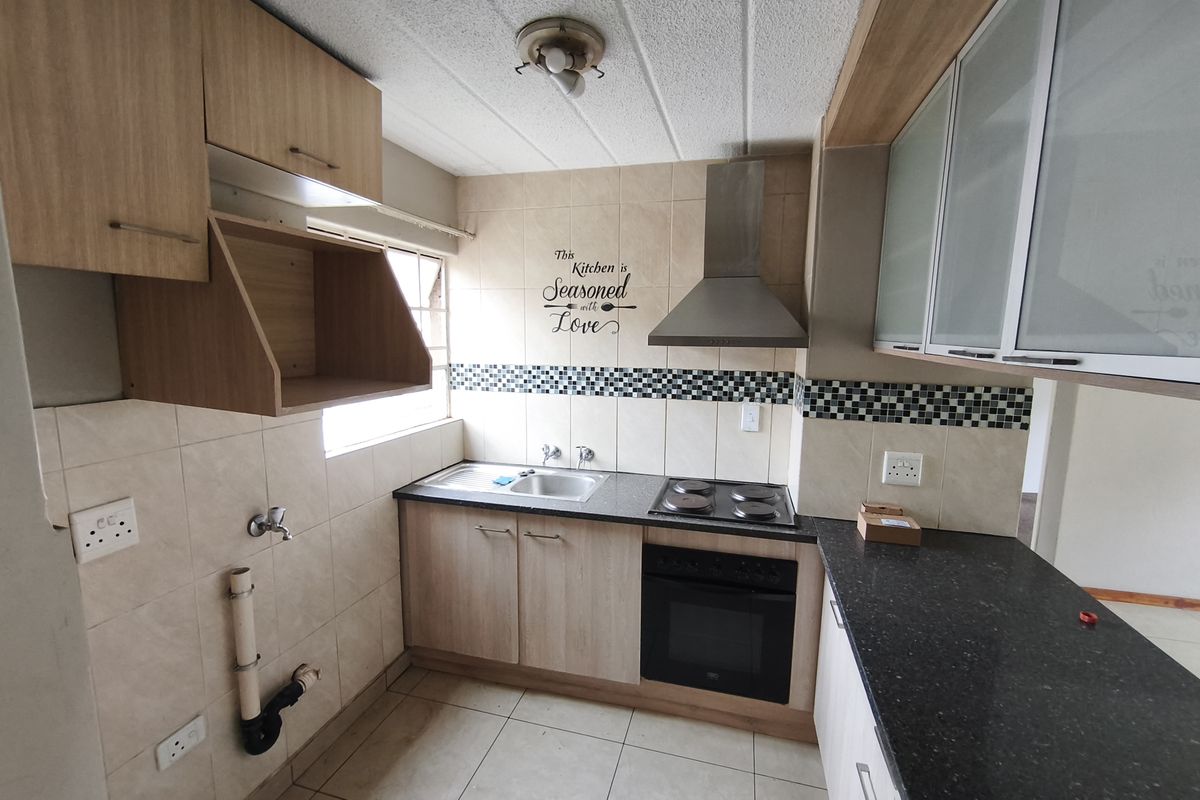 A functional kitchen featuring light wood cabinetry, granite countertops, built-in oven and hob, and tiled backsplash with an exposed plumbing connection.