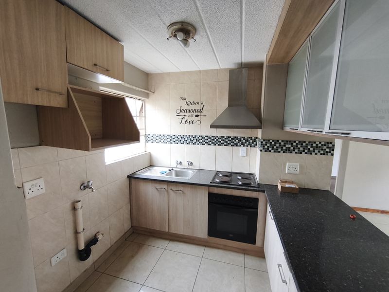 A functional kitchen featuring light wood cabinetry, granite countertops, built-in oven and hob, and tiled backsplash with an exposed plumbing connection.