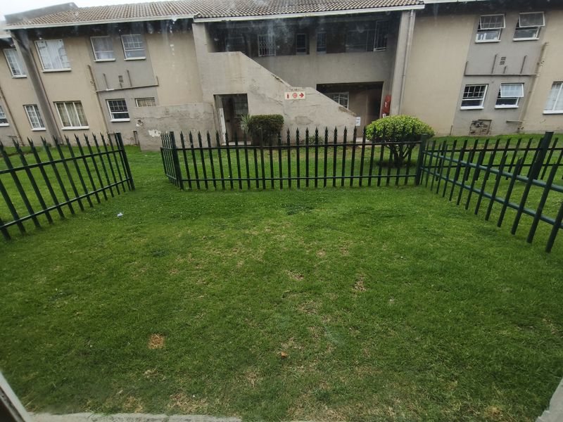 A view of the rear exterior of the apartment complex, featuring a private lawn area enclosed by metal security fencing.