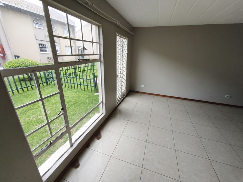 An empty living room featuring tiled flooring, a large window with garden views, and a security gate leading to the exterior.
