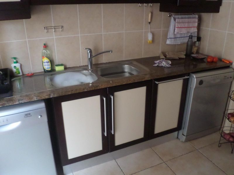 A functional kitchen area featuring a stainless steel double sink, tiled backsplash, and built-in cabinetry with a laminate countertop.