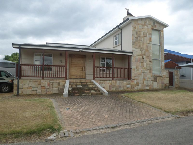 Front elevation of a house featuring stone cladding, a covered porch with timber railings, and a paved driveway.