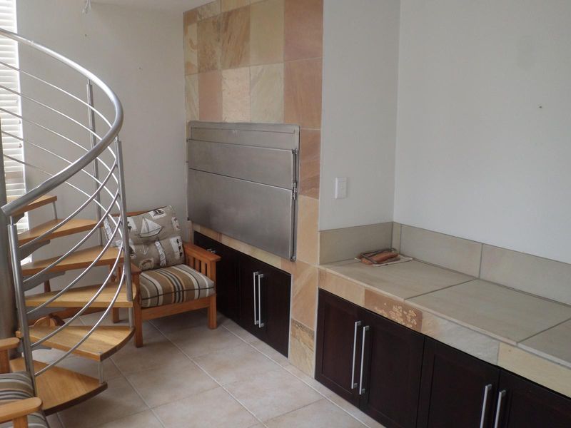 Indoor entertainment area featuring a built-in braai, tiled prep surfaces, dark wood cabinetry, and a modern spiral staircase.
